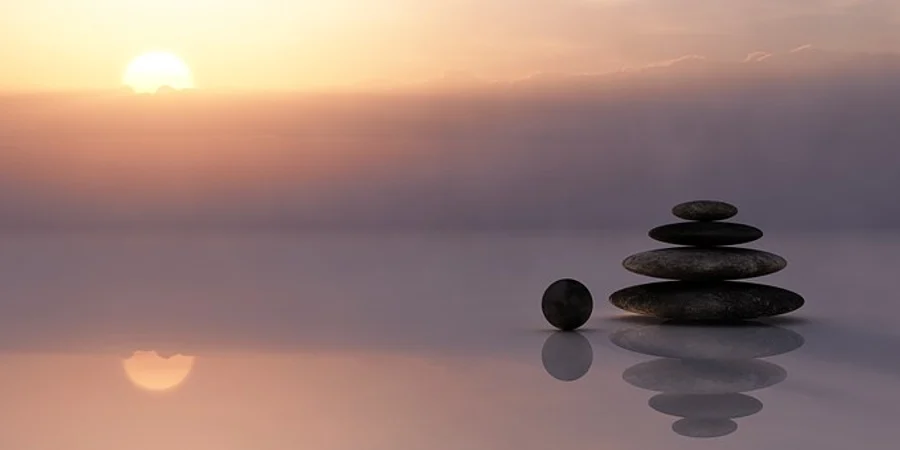 Stacked balancing stones reflected in still water at sunset